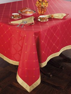 a red table cloth with gold trim on it and silver plates sitting on the table