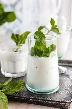 two glasses filled with yogurt and mint garnish on top of a tray