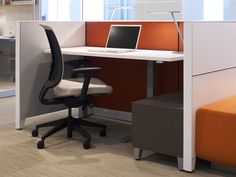 an office cubicle with a laptop on the desk and orange chair next to it