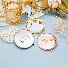 three personalized compact mirrors sitting next to each other on a lace doily with flowers