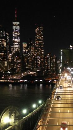 the city skyline is lit up at night as traffic moves along the road in front of it