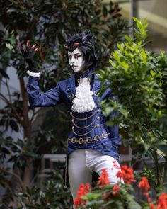 a man dressed in costume standing next to some trees and flowers with his hands out