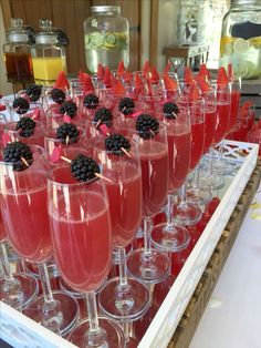 many glasses filled with red liquid and blackberries on top of each other in front of a counter