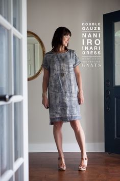 a woman standing in front of a door wearing a dress with buttons on the side