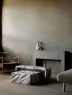 a living room with two chairs and a table in front of a fire place that has a vase on it