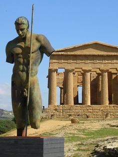 a statue in front of an old building with columns and a man holding a spear