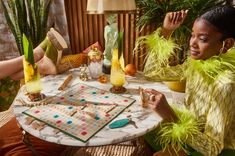 a woman sitting at a table with a board game in front of her and some plants