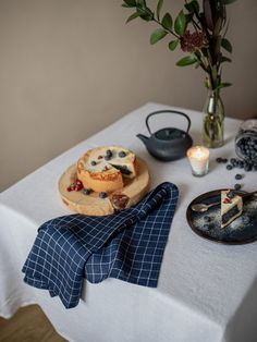 a table topped with plates and cakes on top of a white table cloth next to a vase filled with flowers