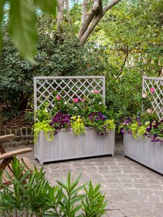 two wooden planters with flowers in them sitting on a brick patio next to trees