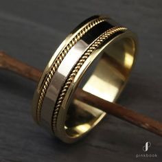 a gold wedding ring with braiding on the side and a wooden stick next to it