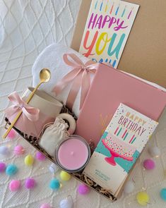 a birthday gift basket with candles, cards and other items on a bed covered in confetti