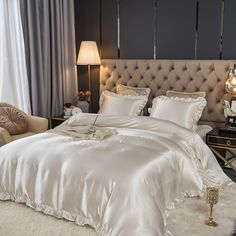 a bed with white comforter and pillows in a bedroom next to a chair, lamp and window