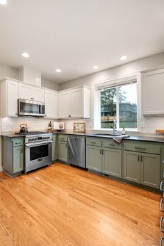 an empty kitchen with wood floors and white cabinets in the middle, along with stainless steel appliances