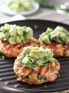 three crab cakes with guacamole on top are sitting on a grill grate