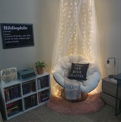 a white chair sitting under a sheer curtain in a living room next to a book shelf