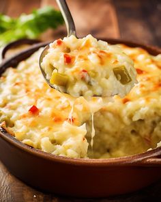 a spoon full of mashed potatoes being lifted from a casserole dish on a wooden table