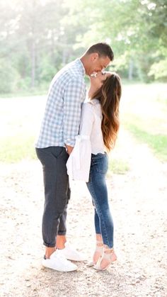 a man and woman standing next to each other on a dirt road with trees in the background