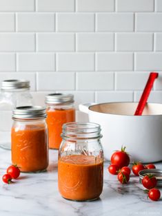 three mason jars filled with tomato sauce on top of a counter next to some tomatoes