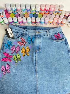 a denim skirt with butterflies painted on it next to paint tubes and markers in the background