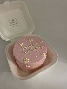 a pink cake in a plastic container with the words happy birthday written on it and daisies