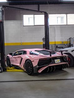 a pink sports car parked in a garage next to a white and black lamb svr