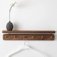 a wooden coat rack with three hooks and a vase on the top, hanging from a white wall