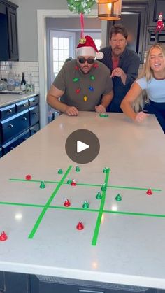 three people standing around a table with christmas decorations on it and one person wearing a santa hat