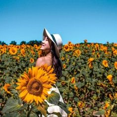 a woman standing in a field of sunflowers with a hat on her head