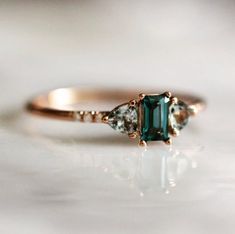 an emerald and diamond three stone ring on a white surface with the top half in yellow gold