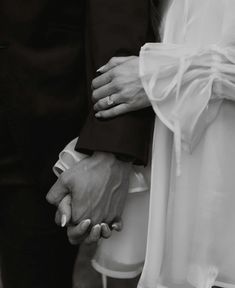 the bride and groom hold hands as they stand close to each other in black and white