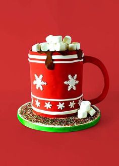 a red mug filled with marshmallows on top of a green plate next to a red wall