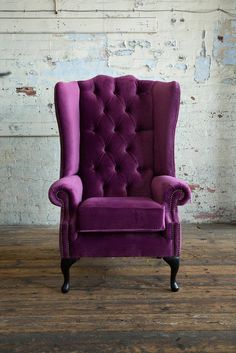 an upholstered purple chair in front of a white brick wall and wooden floor