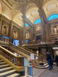 two people are standing at the top of some stairs in a building with ornate architecture