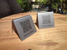 two square coasters sitting on top of a wooden table next to each other with qr code printed on them