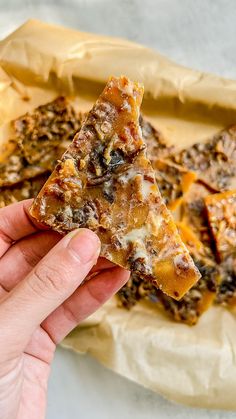 a hand holding up a piece of pizza on top of parchment paper with toppings