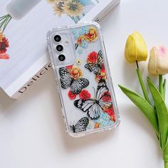 an iphone case with butterflies and flowers on it next to tulips, book and flower