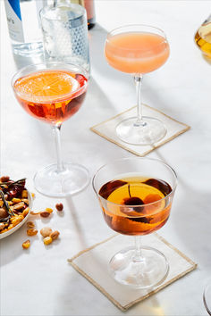 three glasses filled with different types of drinks on top of a white tablecloth covered table