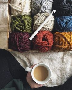 a person holding a cup of coffee in front of yarn