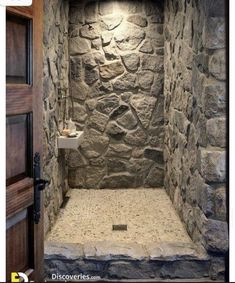 a bathroom with stone walls and flooring is shown in this image, the shower stall has an open door