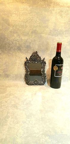 a bottle of wine sitting next to a small mirror on a white tablecloth covered surface