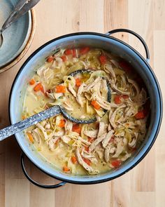 a pot filled with chicken noodle soup on top of a wooden table next to a spoon