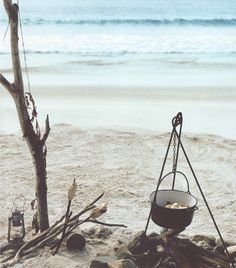 an empty pot is sitting on the beach next to a fire pit and some branches