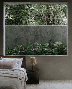 a bed sitting under a window next to a forest filled with green plants and trees