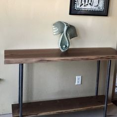 a wooden table with metal legs and a vase on top in front of a white wall