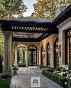 the entrance to a large home with lots of greenery and bushes on either side