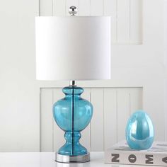 a blue lamp sitting on top of a table next to a book and a white shade