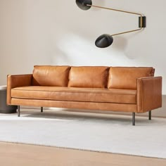 a tan leather couch sitting on top of a white rug next to a wall mounted lamp