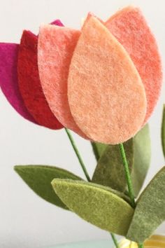 three felt flowers in a vase with green leaves on the top and one pink flower on the bottom