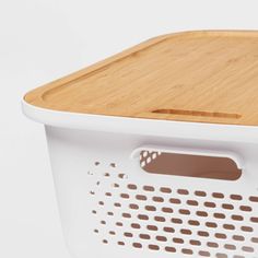 a wooden cutting board sitting on top of a white basket with holes in the bottom