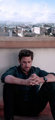 a man sitting on top of a building next to a wall with his hands crossed